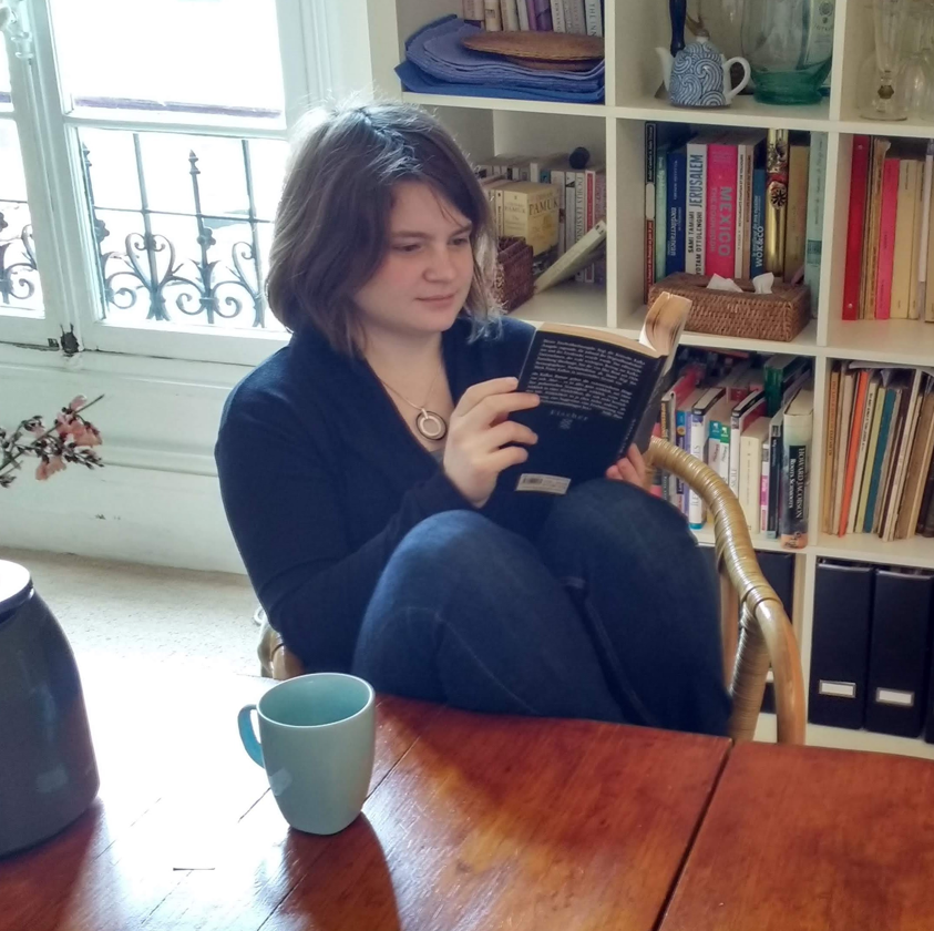 Kris reading at home beside a bookshelf