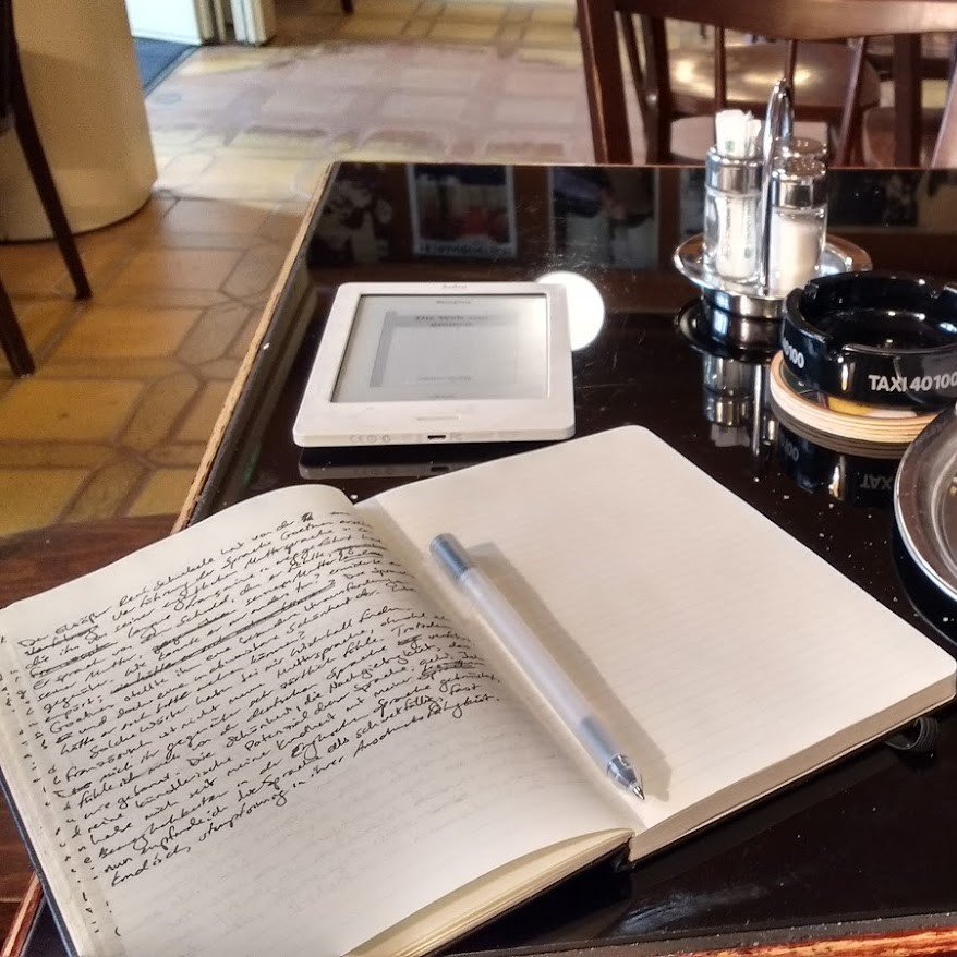An open notebook and e-reader on a café table